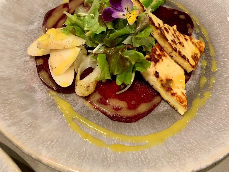 A plated first course: beet carpaccio with seared cheese, avocado and greens