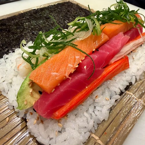 A sushi roll being made with salmon and tuna